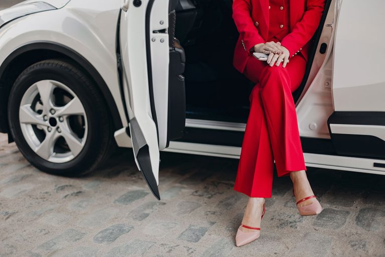 Mulher com roupas elegantes, sentada em um carro de luxo com a porta aberta